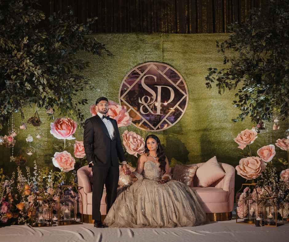 Bride and Groom on reception stage with oversized flowers and a green moss wall