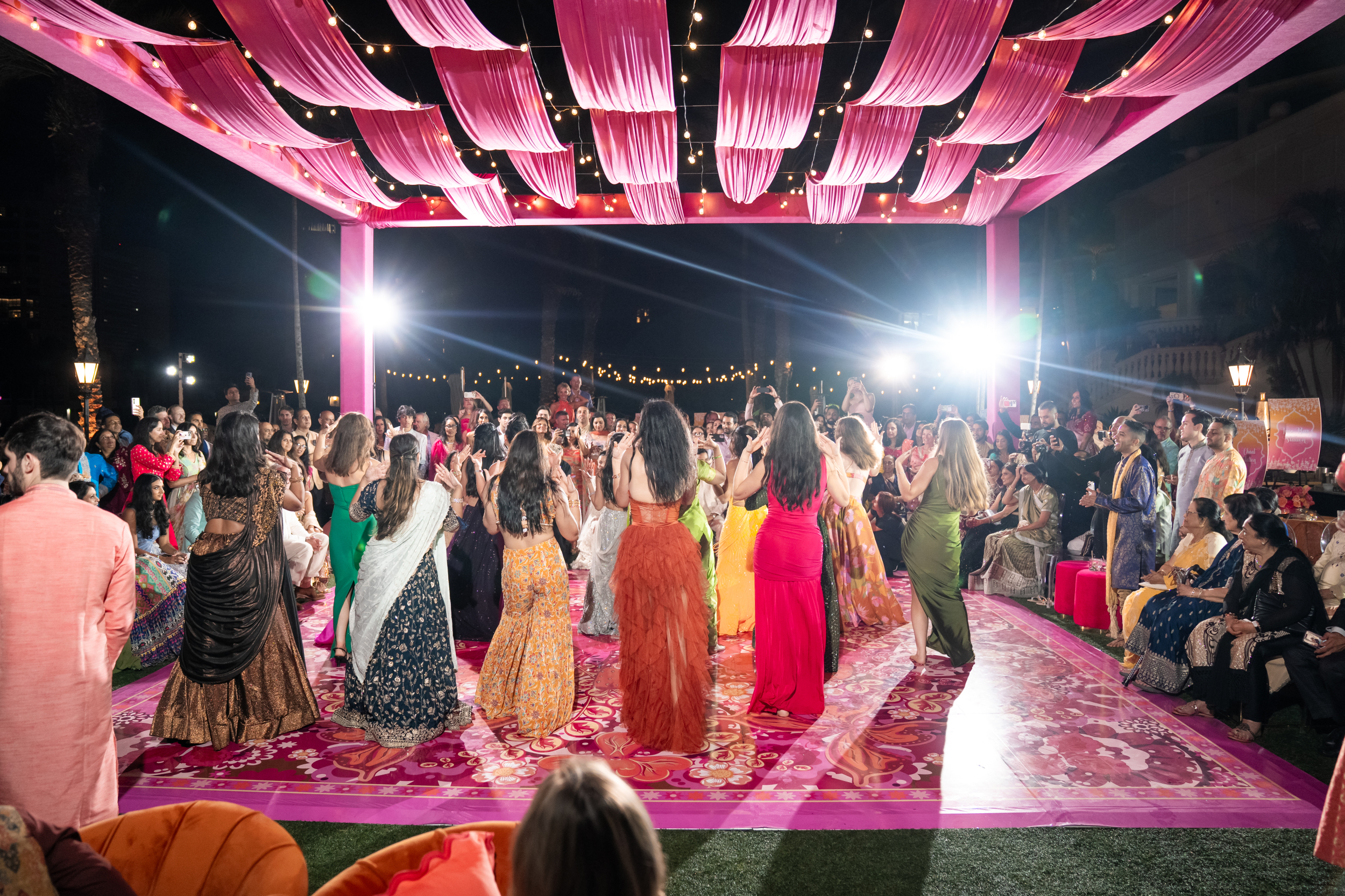 Sangeet Dance performance at night under a pink canopy and palm trees.