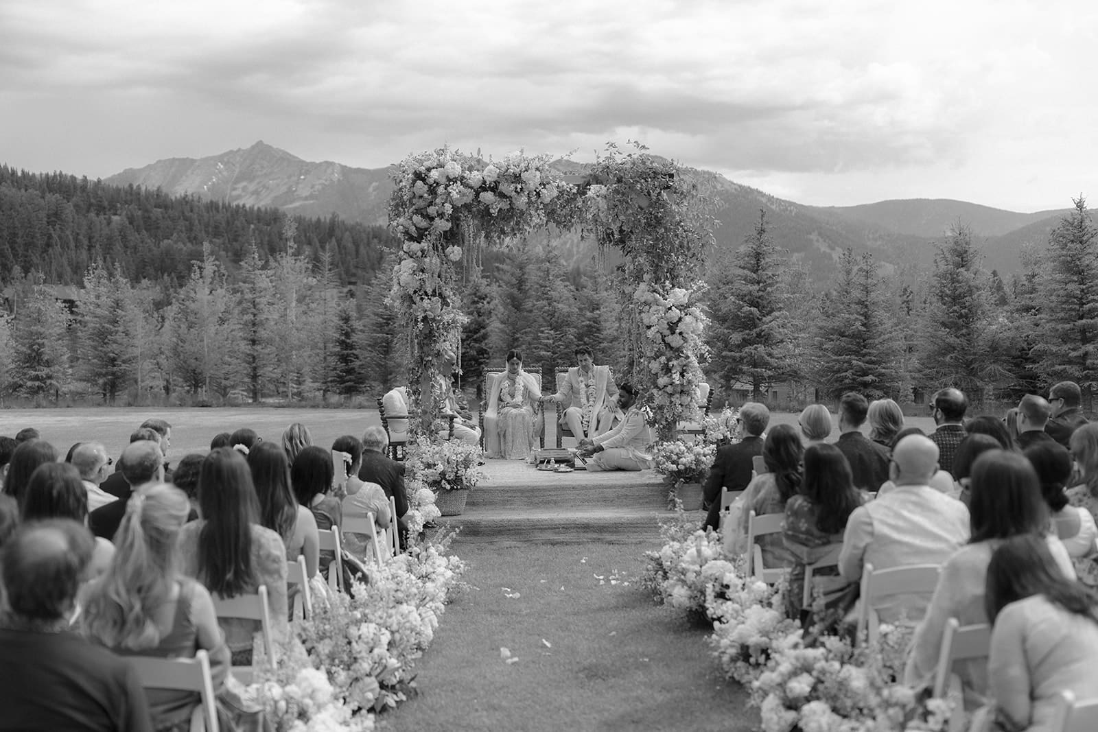 Bride and groom exchange vows beneath a floral Hindu wedding mandap with the Rocky Mountains as the backdrop during an outdoor luxury South Asian destination wedding at Montage Big Sky in Montana.